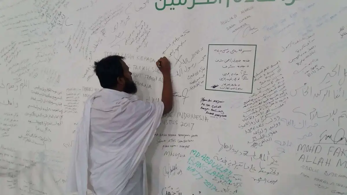 একজন ব্যক্তি বড় দেয়ালে স্বাক্ষর করছেন, বিভিন্ন লেখা ও স্বাক্ষর দিয়ে ভরা. Channel i News - চ্যানেল আই নিউজ