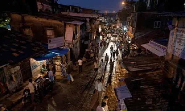 বস্তি এলাকার রাস্তায় সন্ধ্যায় মানুষের চলাচল, আলো ও অন্ধকারের সংমিশ্রণে দৃশ্য. Channel i News - চ্যানেল আই নিউজ