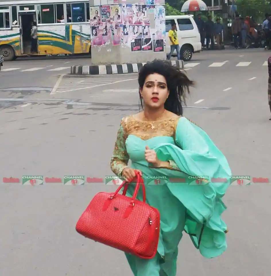 মাহি দৌড়াচ্ছেন ব্যস্ত শহরে, পেছনে বাস ও পথচারী।. Channel i News - চ্যানেল আই নিউজ