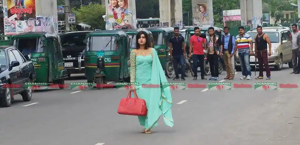মাহি ব্যস্তভাবে রাস্তা পার হচ্ছেন, পাশে লোকজন দাঁড়িয়ে আছে. Channel i News - চ্যানেল আই নিউজ