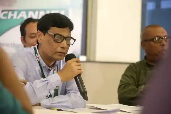 একজন সাংবাদিক সংবাদ সম্মেলনে বক্তব্য দিচ্ছেন, অন্যরা শুনছেন. Channel i News - চ্যানেল আই নিউজ