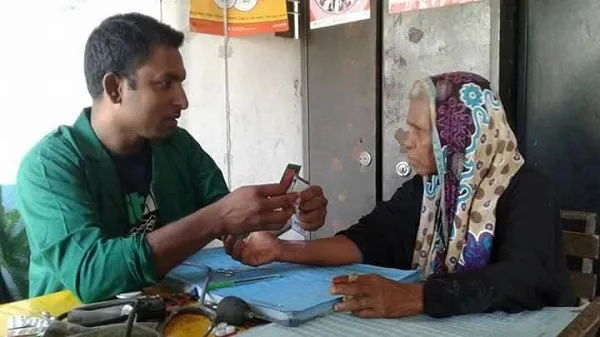 স্বাস্থ্যসেবা প্রদানকারী একজন যুবক বৃদ্ধার হাতে রক্তচাপ পরিমাপ করছেন।. Channel i News - চ্যানেল আই নিউজ