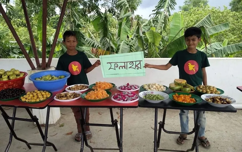 দুটি শিশু স্বপ্ননগর বিদ্যানিকেতনের শিক্ষার্থী, ফলমূল ও খাবার সাজানো টেবিলে. Channel i News - চ্যানেল আই নিউজ