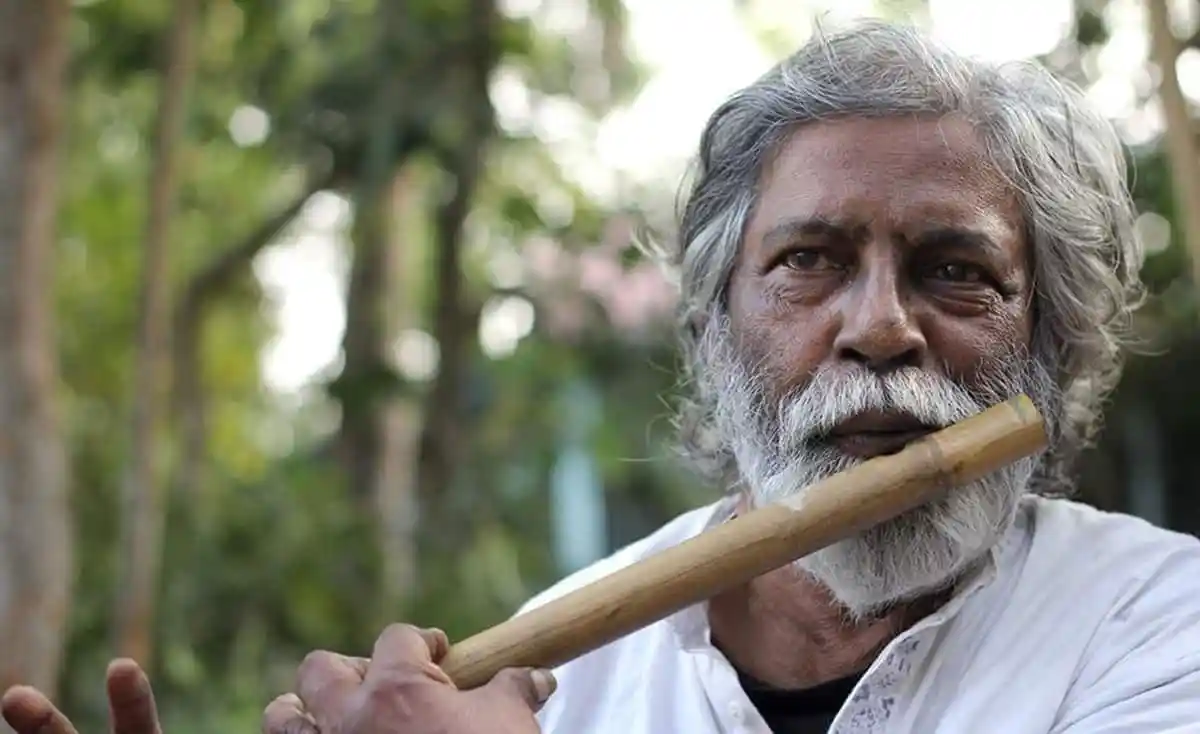 বৃদ্ধ ব্যক্তি বাঁশি বাজাচ্ছেন, প্রকৃতি পেছনে. Channel i News - চ্যানেল আই নিউজ