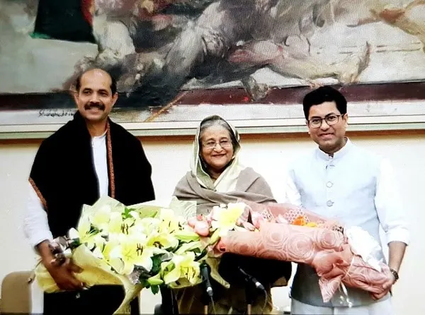 তিনজন ব্যক্তি ফুলের তোড়া নিয়ে হাসিমুখে দাঁড়িয়ে আছেন।. Channel i News - চ্যানেল আই নিউজ