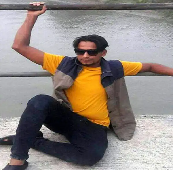 Man sitting by riverbank wearing sunglasses and yellow shirt. Channel i News - চ্যানেল আই নিউজ