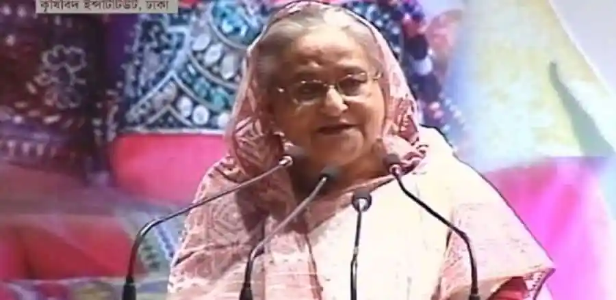 প্রধানমন্ত্রী শেখ হাসিনা ভাষণ দিচ্ছেন, পেছনে জনসমাগম।. Channel i News - চ্যানেল আই নিউজ