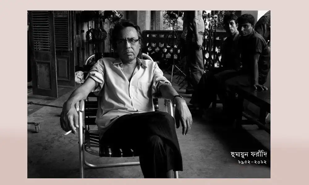 হুমায়ুন ফরীদি বসে আছেন, পেছনে কিছু মানুষ দাঁড়িয়ে রয়েছে. Channel i News - চ্যানেল আই নিউজ