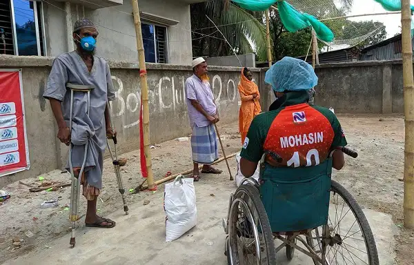 প্রতিবন্ধী ব্যক্তি wheelchair এ বসে, অন্যরা সামাজিক দূরত্বে দাঁড়িয়ে. Channel i News - চ্যানেল আই নিউজ
