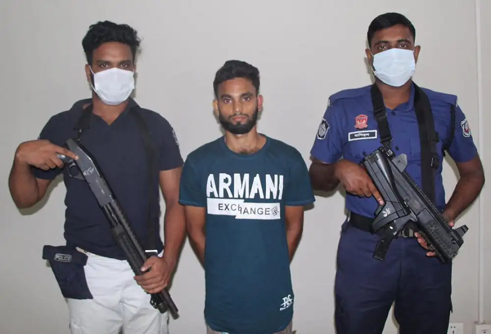 Two armed police officers with a man in the middle, all wearing masks. Channel i News - চ্যানেল আই নিউজ