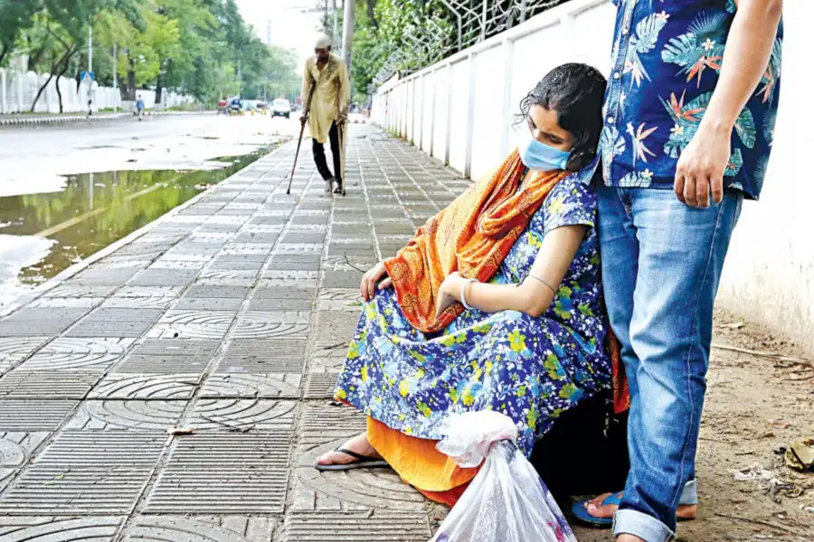 বৃষ্টির পরে রাস্তার পাশে বসে থাকা একজন নারী ও তার পাশে দাঁড়ানো একজন পুরুষ. Channel i News - চ্যানেল আই নিউজ