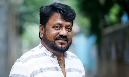 বাংলাদেশি পুরুষের ছবি, হালকা হাসি ও গা dark ় রঙের শার্ট পরা. Channel i News - চ্যানেল আই নিউজ