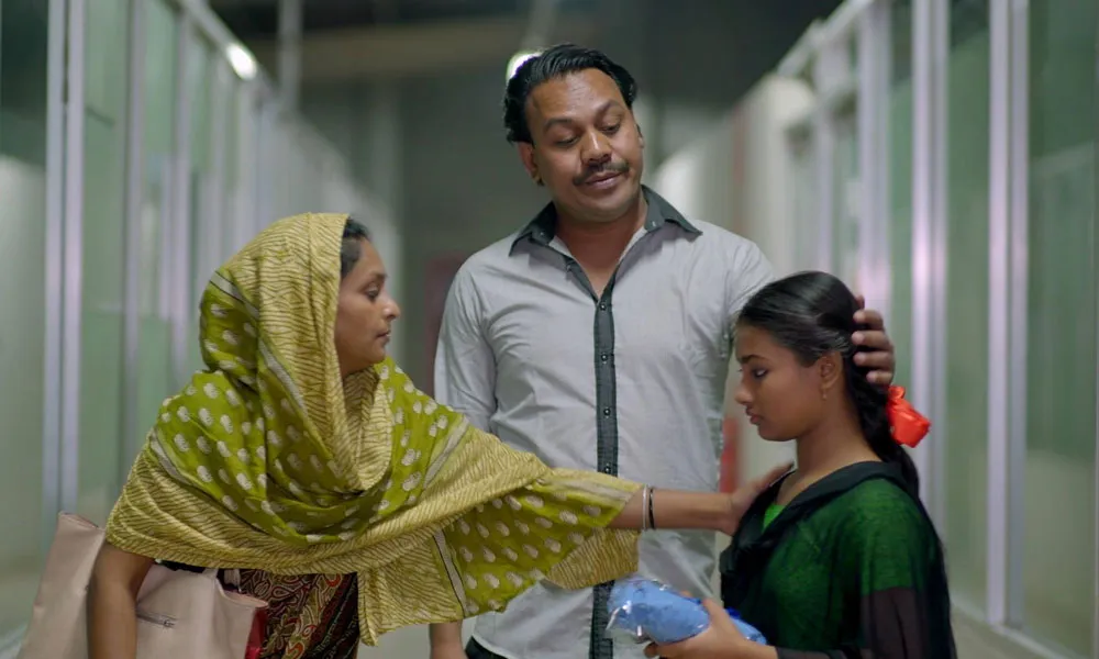 একটি ছোট মেয়ে তার মা ও বাবার সাথে হাসপাতালে বসে আছে. Channel i News - চ্যানেল আই নিউজ