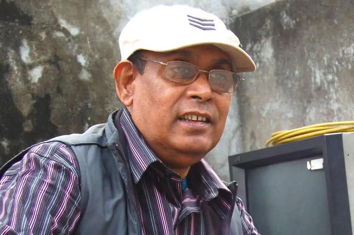 বাংলাদেশের একজন সংবাদ প্রতিবেদক, ক্যাপ, চশমা পরা, পটভূমিতে কংক্রিট দেয়াল. Channel i News - চ্যানেল আই নিউজ