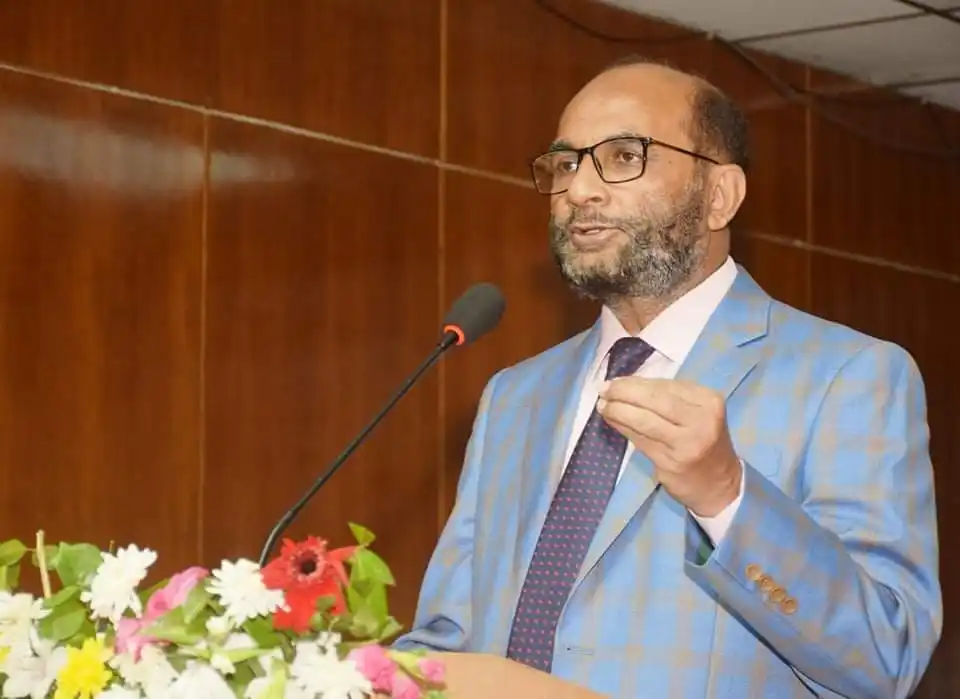 বাংলাদেশি ব্যক্তি বক্তৃতা দিচ্ছেন, পেছনে গাছের ফুলের সাজ. Channel i News - চ্যানেল আই নিউজ