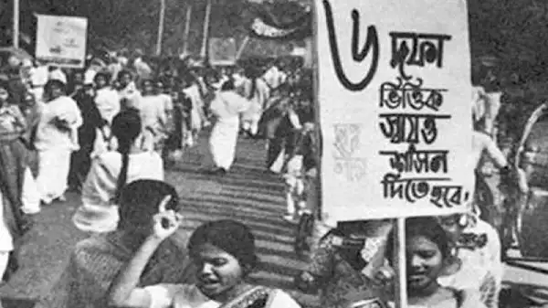 বিক্ষোভকারীরা রাস্তায় দাঁড়িয়ে প্রতিবাদ জানাচ্ছেন, একটি পোস্টার ধরে।. Channel i News - চ্যানেল আই নিউজ