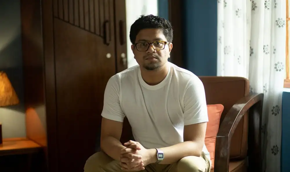 আত্মবিশ্বাসী যুবক বসে আছেন ঘরে, ক্যামেরার দিকে তাকিয়ে।. Channel i News - চ্যানেল আই নিউজ