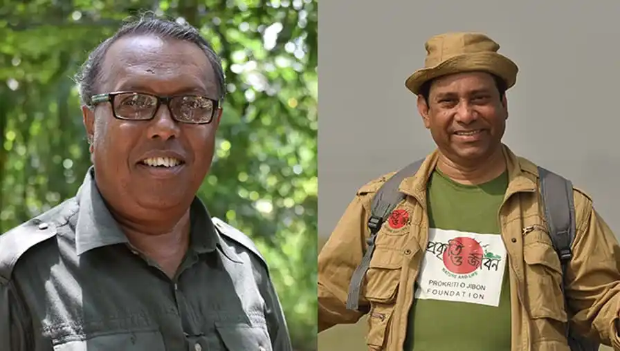 Two men smiling, one in glasses and a black shirt, the other in a hat and khaki jacket. Channel i News - চ্যানেল আই নিউজ