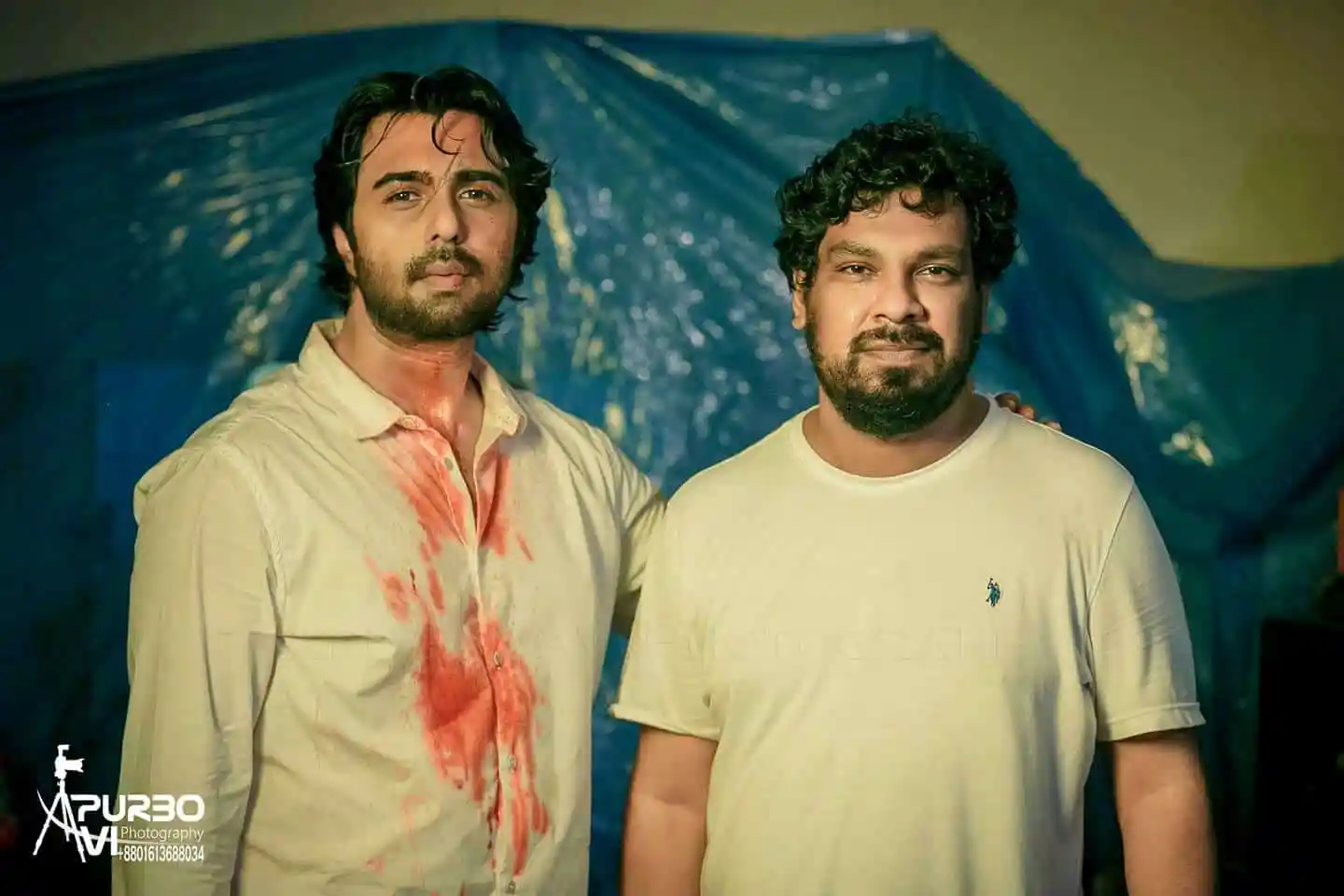 দুই যুবক বন্ধু ক্যামেরার সামনে দাঁড়িয়ে, পেছনে নীল টেন্ট।. Channel i News - চ্যানেল আই নিউজ