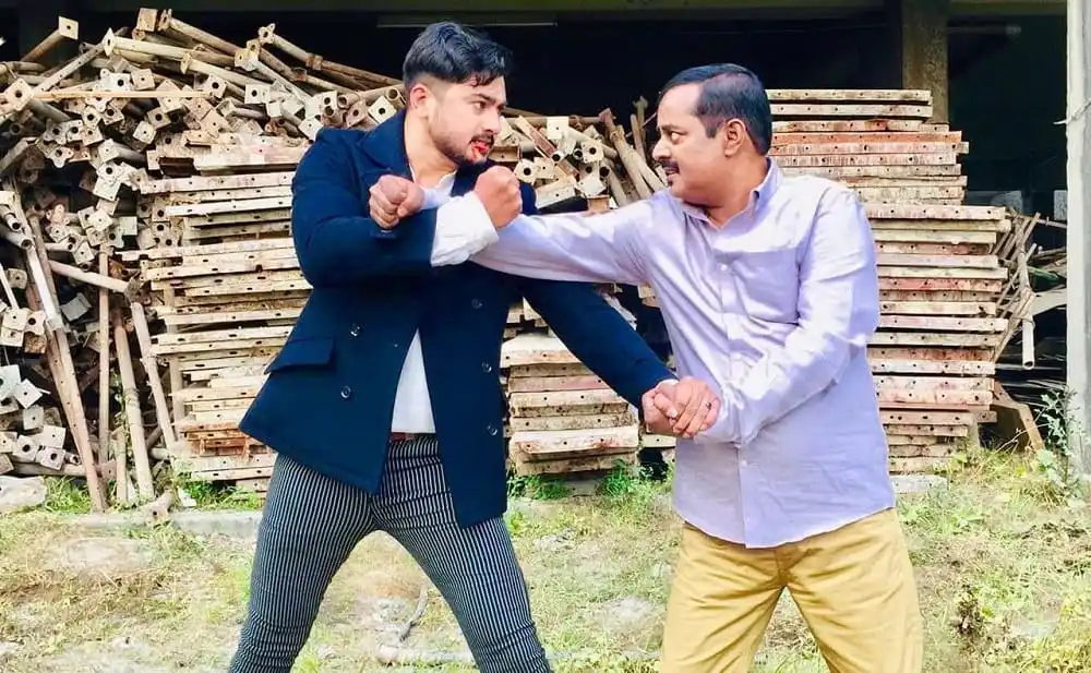 দুই ব্যক্তি মারামারি করছে, পেছনে কাঠের স্তূপ।. Channel i News - চ্যানেল আই নিউজ