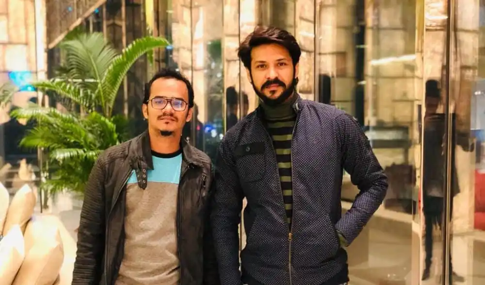 দুই ব্যক্তি হাসিমুখে দাঁড়িয়ে, আধুনিক ভবনের সামনে. Channel i News - চ্যানেল আই নিউজ