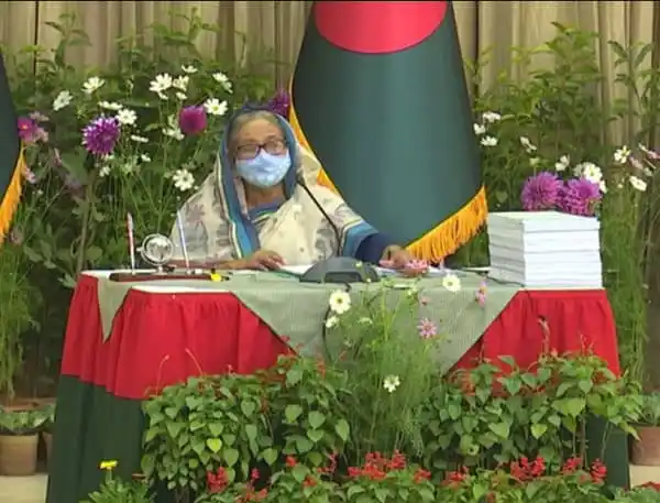 প্রধানমন্ত্রী বৈঠকে বসে, পাশে বাংলাদেশের পতাকা ও ফুলের সাজসজ্জা. Channel i News - চ্যানেল আই নিউজ