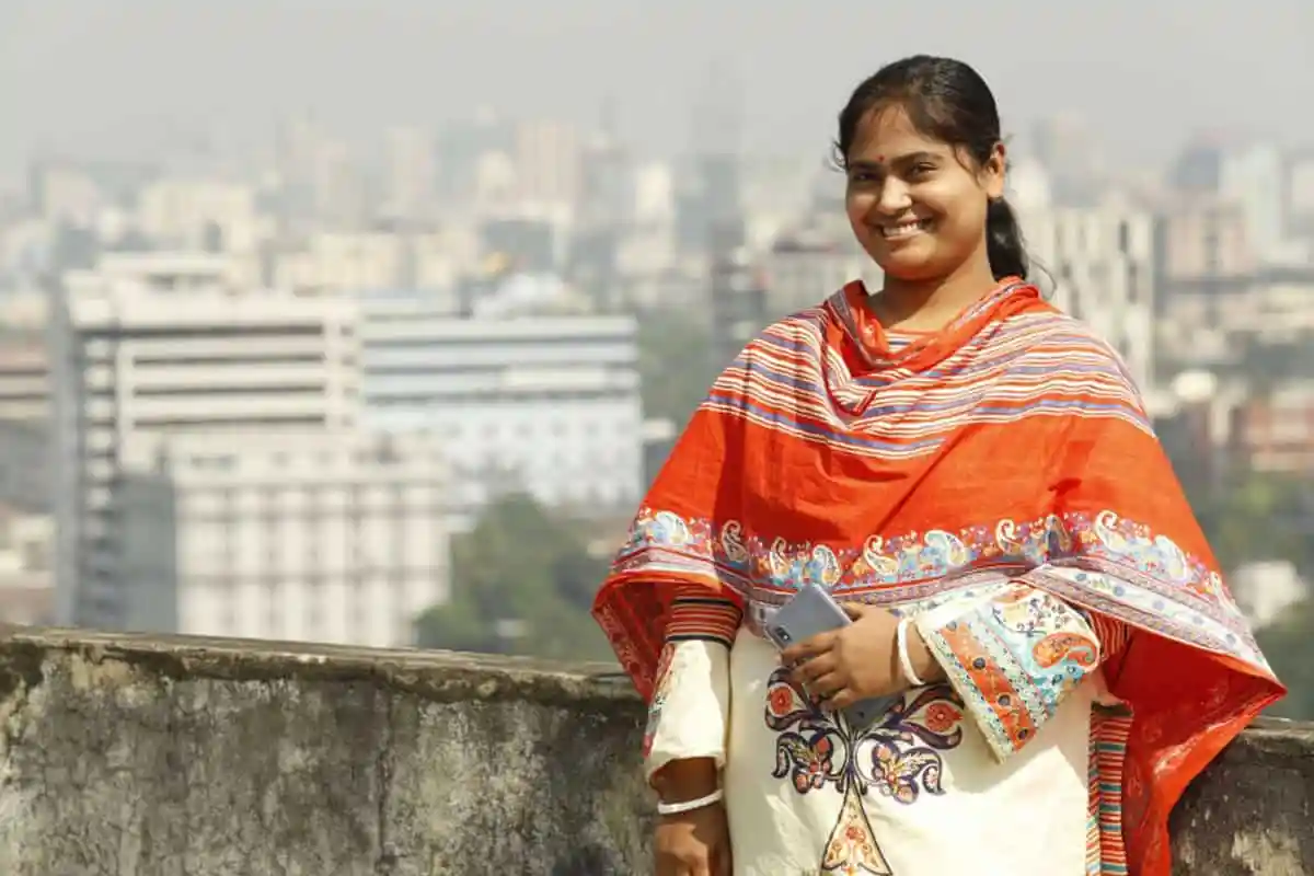 প্রভার হাসিমুখে রঙিন শাড়ি পরা, শহরের ব্যাকড্রপের সামনে. Channel i News - চ্যানেল আই নিউজ