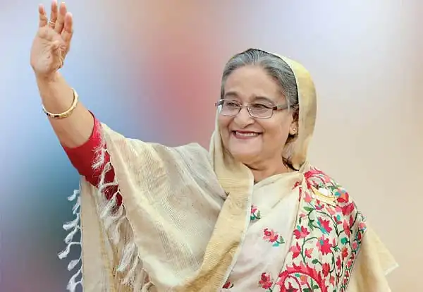 শেখ হাসিনা waving with a smile, wearing traditional attire and glasses. Channel i News - চ্যানেল আই নিউজ