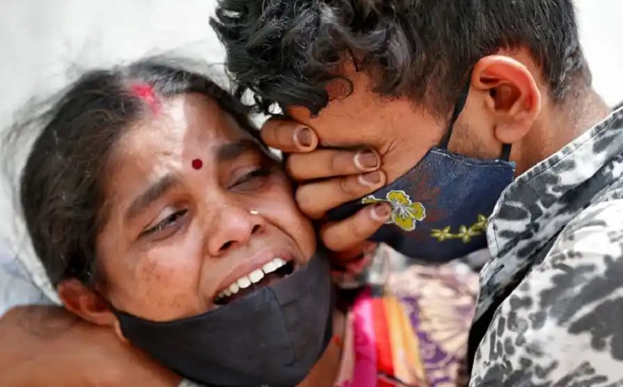 দুজন ব্যক্তি কাঁদছেন, একে অপরকে জড়িয়ে ধরে, মুখে মাস্ক পরা।. Channel i News - চ্যানেল আই নিউজ