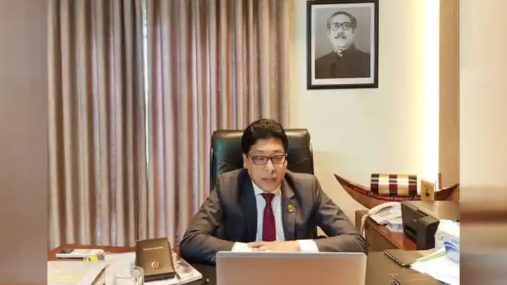 অফিসে বসে কাজ করছেন একজন সরকারি কর্মকর্তা, পেছনে বঙ্গবন্ধুর ছবি. Channel i News - চ্যানেল আই নিউজ