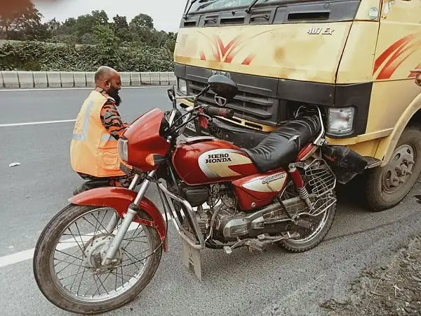 Motorcycle accident scene with a man inspecting the damaged bike near a truck. Channel i News - চ্যানেল আই নিউজ
