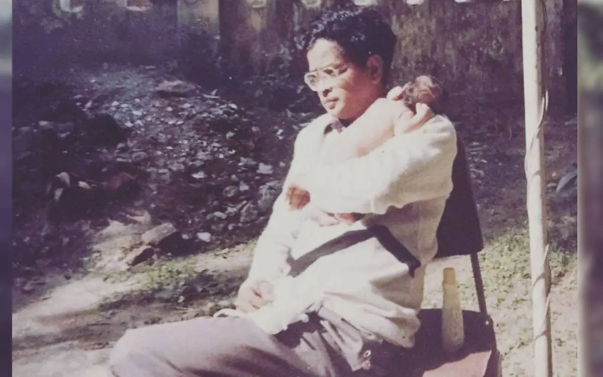 A young man sitting outdoors with a small dog on his lap, wearing glasses and a white sweater. Channel i News - চ্যানেল আই নিউজ