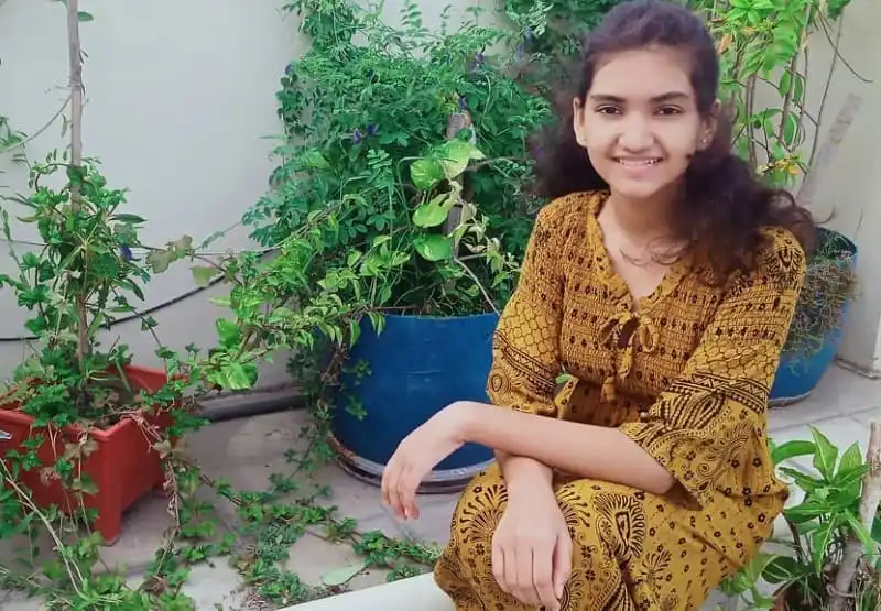 Smiling young woman in traditional dress sitting among potted plants. Channel i News - চ্যানেল আই নিউজ