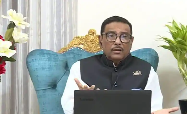 বাংলাদেশের একজন নেতা অনলাইনে বক্তব্য দিচ্ছেন, পটভূমিতে ফুলের গাছ ও আসবাব।. Channel i News - চ্যানেল আই নিউজ