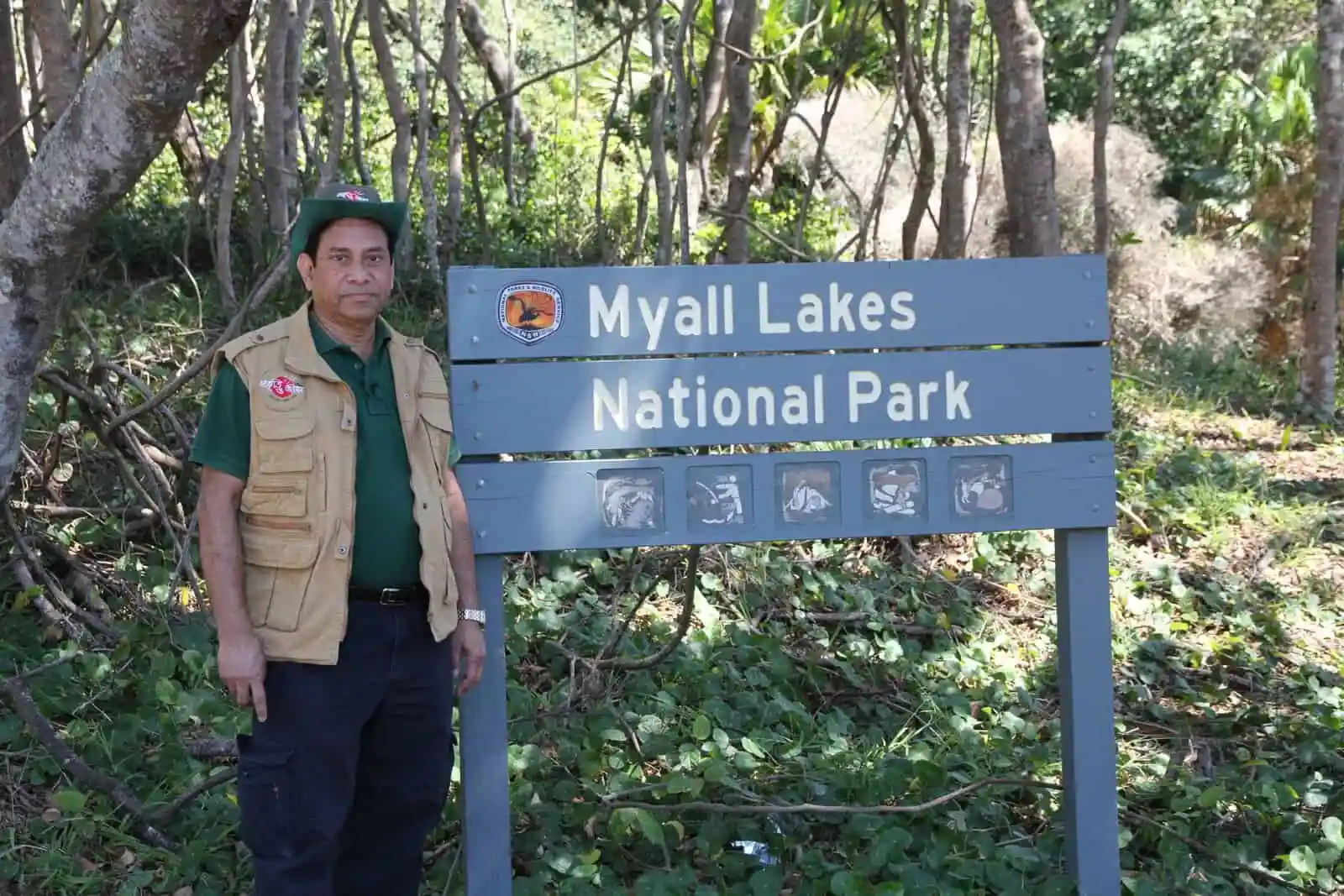 Man standing beside Myall Lakes National Park sign in lush forest. Channel i News - চ্যানেল আই নিউজ