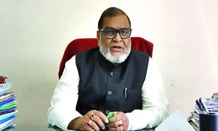 বাংলাদেশের একজন নেতা বসে আছেন, পেছনে সাদা দেয়াল ও ডেস্ক. Channel i News - চ্যানেল আই নিউজ