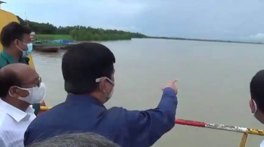 নদীর পাশে বসে কিছু মানুষ সেতুর নির্মাণ কাজ দেখছেন. Channel i News - চ্যানেল আই নিউজ