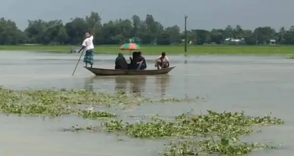 তিনজন মানুষ পানিতে ভাসমান নৌকায়, একজন দাঁড়িয়ে আছেন, অন্যরা বসে আছেন. Channel i News - চ্যানেল আই নিউজ