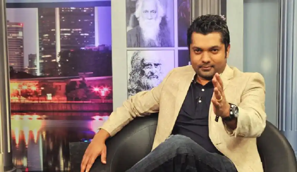 চ্যানেল আই অনলাইন এর সাংবাদিকের ছবি, তিনি বসে আছেন, পেছনে শহরের দৃশ্য ও বিখ্যাত ব্যক্তির ছবি. Channel i News - চ্যানেল আই নিউজ