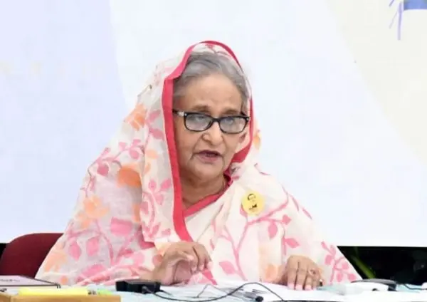 Bangladeshi woman in traditional saree and glasses speaking at a press conference. Channel i News - চ্যানেল আই নিউজ