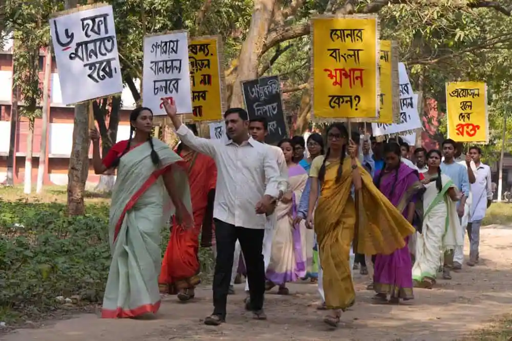 বিভিন্ন মানুষ প্রতিবাদে অংশগ্রহণ করছে, হাতে প্ল্যাকার্ড নিয়ে. Channel i News - চ্যানেল আই নিউজ