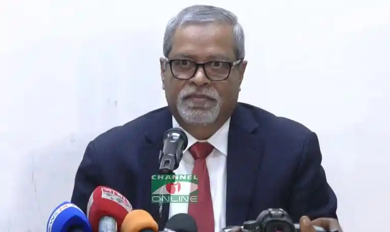 Bangladeshi man in suit speaking at a press conference with microphones. Channel i News - চ্যানেল আই নিউজ