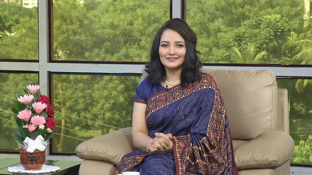 উপস্থাপিকা মুনমুনের ছবি, তিনি বসে আছেন, হাসছেন, পেছনে সবুজ গাছের দৃশ্য।. Channel i News - চ্যানেল আই নিউজ