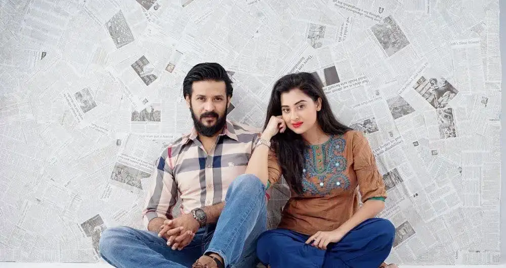দুটি যুবক-যুবতী সংবাদপত্রের পেছনে বসে ছবি তুলছেন।. Channel i News - চ্যানেল আই নিউজ