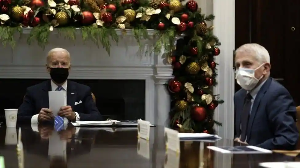 Two men wearing masks sit at a table decorated for Christmas. Channel i News - চ্যানেল আই নিউজ