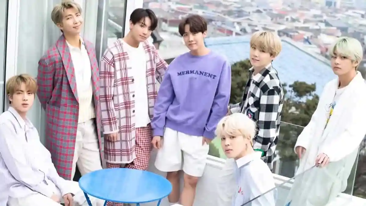BTS members in casual attire during a photoshoot on a balcony. Channel i News - চ্যানেল আই নিউজ