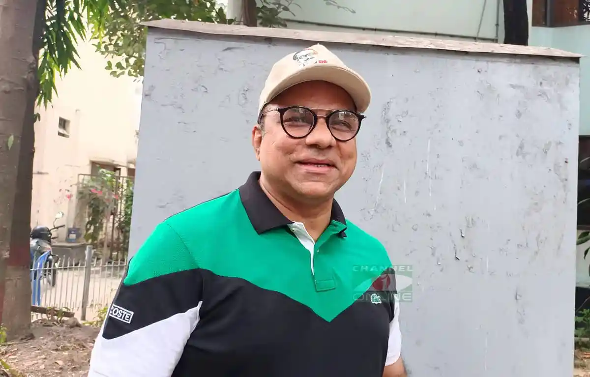 Smiling man wearing glasses and a green and black polo shirt outdoors. Channel i News - চ্যানেল আই নিউজ