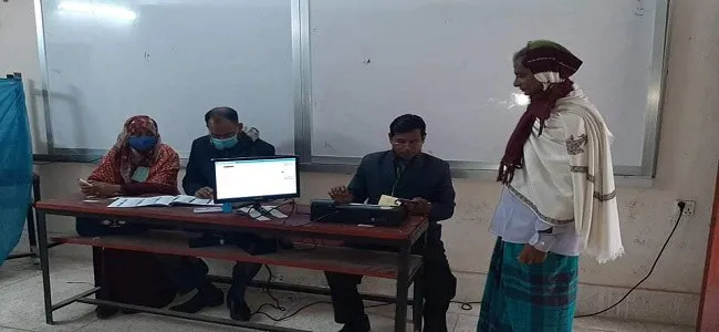 একজন ভোটার ভোট কেন্দ্রে ভোট দিচ্ছেন, অন্যরা কাজের জন্য বসে আছেন. Channel i News - চ্যানেল আই নিউজ