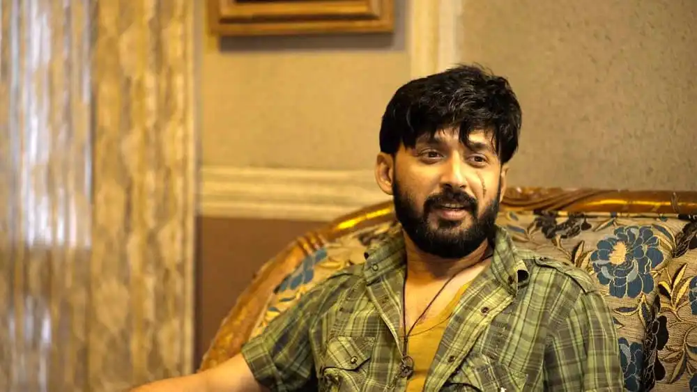দোদুলের চরিত্রে অভিনেতা একটি সোফায় বসে হাসছেন. Channel i News - চ্যানেল আই নিউজ