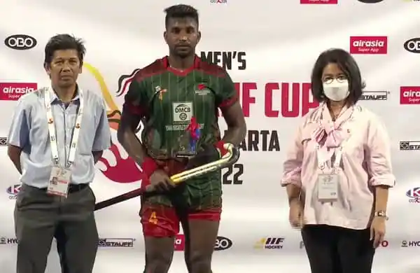 Bangladeshi hockey player holding a trophy at a sports event. Channel i News - চ্যানেল আই নিউজ